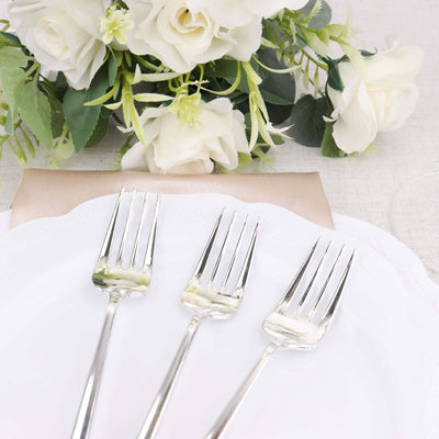 Three silver forks on a white plate, surrounded by white roses.
