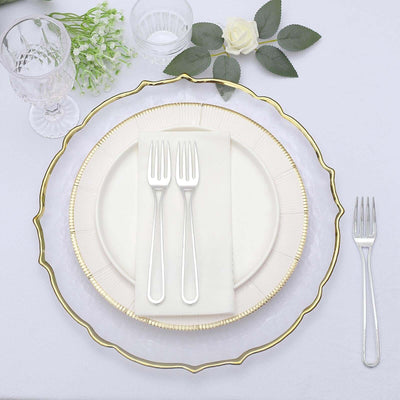 Elegant dining setup with gold-trimmed plates and silver forks on a white tablecloth.