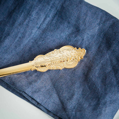 Gold decorative serving spoon on a navy linen napkin.