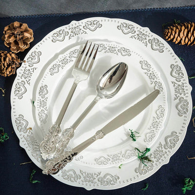 Elegant silverware set on a decorative plate with pinecones and greenery.