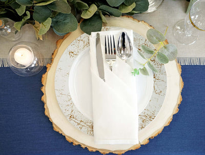 Elegant table setting with a white plate, cutlery, and greenery on a rustic wood charger.