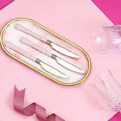 Elegant pink knives on a decorative tray with glassware and ribbon.