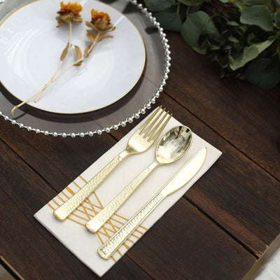 Elegant gold cutlery set on a decorative placemat with a plate and flowers.