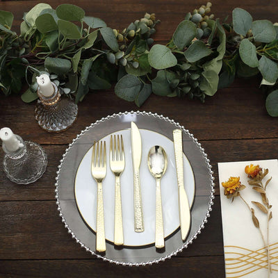 Elegant gold cutlery set on a decorative plate with greenery and candles.