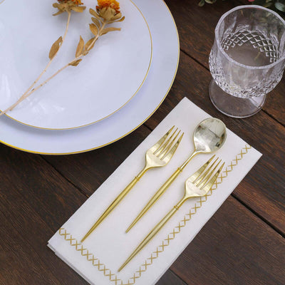 Elegant gold flatware set on a napkin with decorative stitching and fine dining setup.