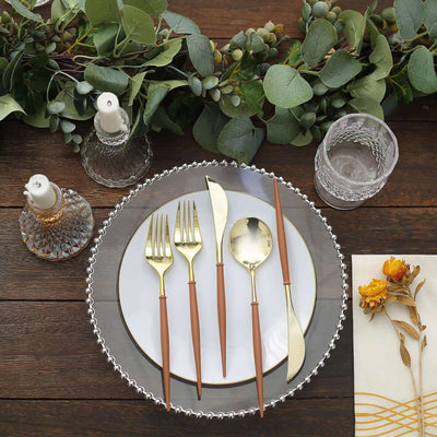 Elegant gold and brown cutlery set on a decorative plate with candles and greenery.