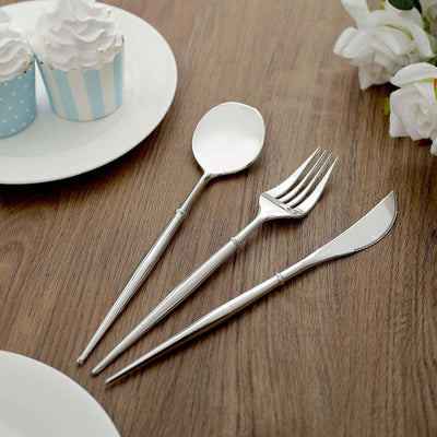 Elegant stainless steel cutlery set on a wooden table with cupcakes.