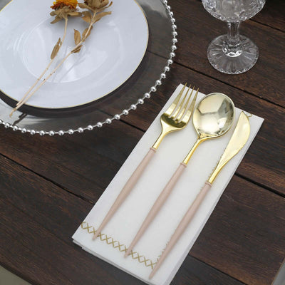 Gold cutlery set on a napkin with decorative plate and glass in a rustic table setting.
