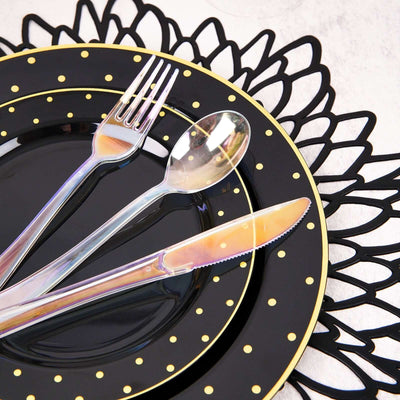 Black and gold polka dot dinnerware set with cutlery on an elegant placemat.