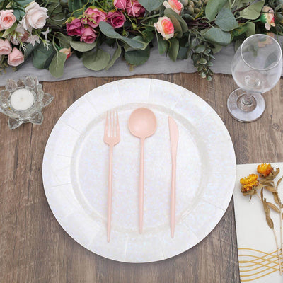 Pink cutlery set on a decorative plate with floral arrangement in the background.
