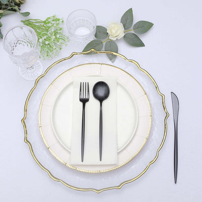 Elegant table setting with gold-rimmed plate, black cutlery, and elegant glassware.