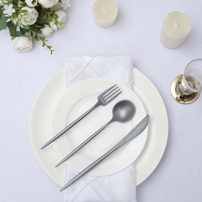 Elegant silver cutlery set on a white plate with napkin and candles.