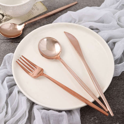 Rose gold cutlery set on a white plate with a soft fabric backdrop.
