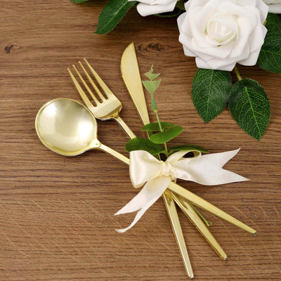 Gold cutlery set with a ribbon and greenery on a wooden table.