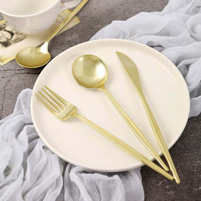 Gold cutlery set on a white plate with a soft fabric backdrop.