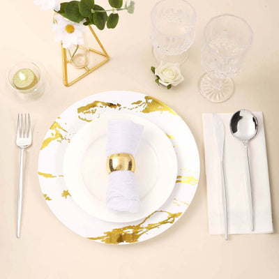 Elegant white plate with gold marbling, napkin, and silver cutlery on a table setting.
