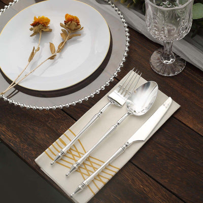 Elegant silver flatware set on a stylish table with decorative plate and flowers.