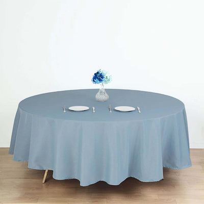 Round blue tablecloth with plates and vase on a wooden table.