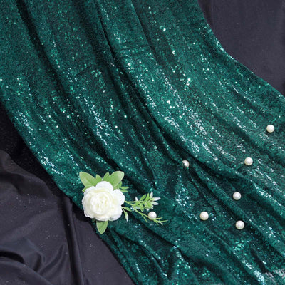Emerald green sequin fabric draped with decorative pearls and a white flower.