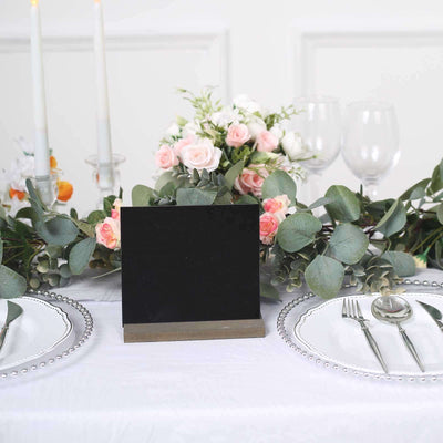 Black tabletop sign holder with floral centerpiece and dinner setting.