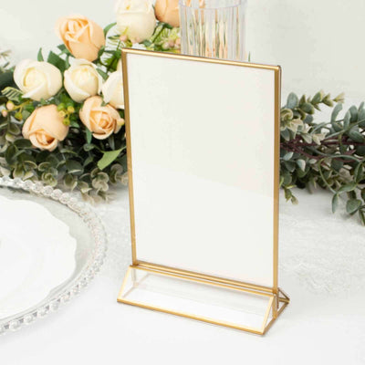 Gold-framed table sign holder with a blank insert on a floral backdrop.