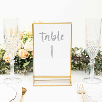 Table number sign with gold frame, surrounded by elegant glassware and floral decor.