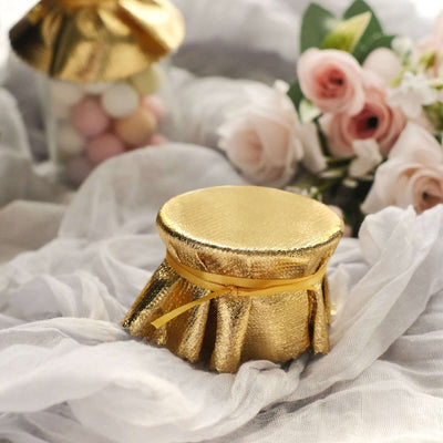 Gold decorative jar with a ribbon, surrounded by soft fabrics and flowers.