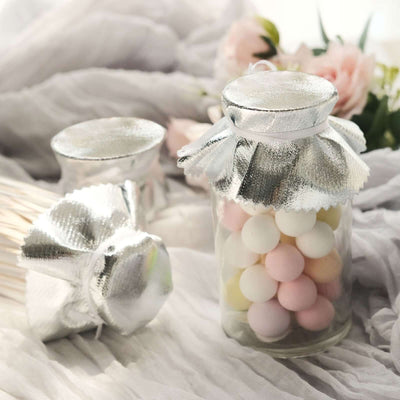 Glass jars with pastel candy and silver lids on a soft textured background.