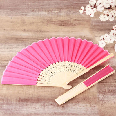 Pink folding fan displayed on a wooden surface with decorative flowers.