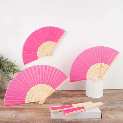 Pink decorative fans displayed on a wooden surface with a white vase.
