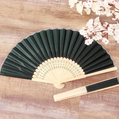 Black folding fan with bamboo handle on wooden surface.