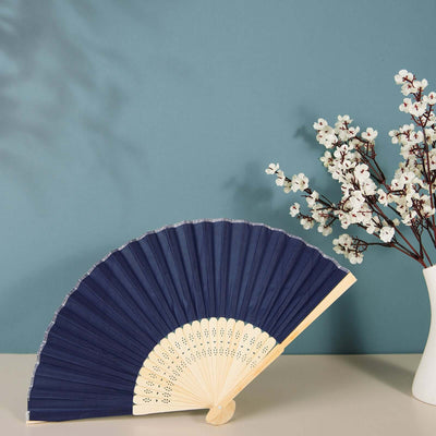 Navy blue folding fan with wooden handle next to a vase of flowers.