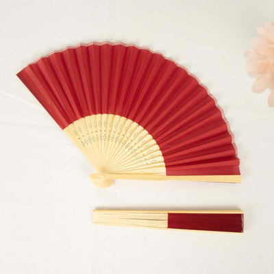 Red folding fan with bamboo handle on a plain backdrop.