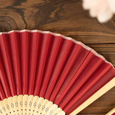 Red folding fan on a wooden surface.