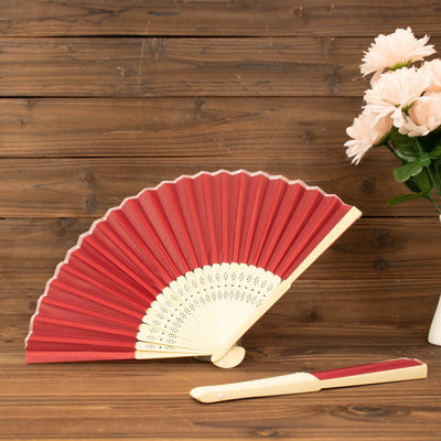 Red decorative fan with cream accents beside a vase of pink flowers.