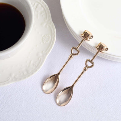 Elegant gold teaspoons beside a coffee cup and white plates.