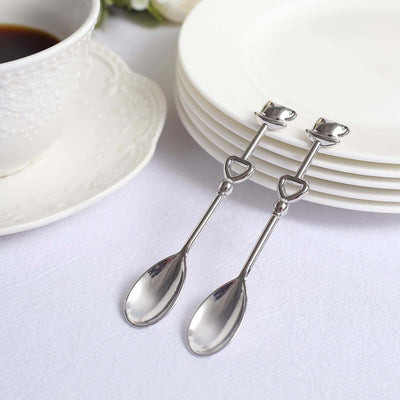 Elegant silver dessert spoons beside white plates and a cup of coffee.