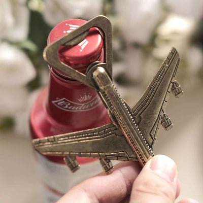 Airplane-shaped bottle opener in hand with a beverage in the background.