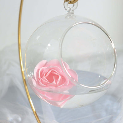 Glass hanging terrarium with pink flower and water.