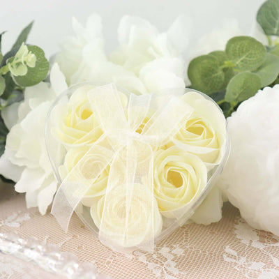 Heart-shaped box of ivory roses with a ribbon, surrounded by soft floral decor.