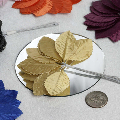 Gold textured fabric leaves arranged on a mirror with colorful leaves in the background.