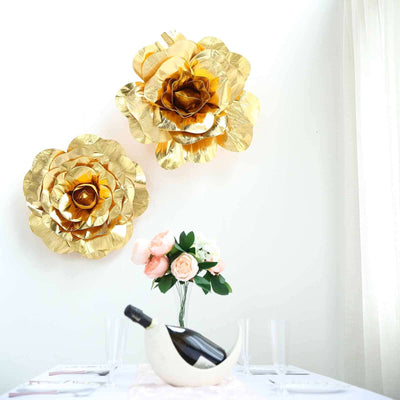 Gold paper flowers displayed on a white wall with a floral arrangement and wine bottle.