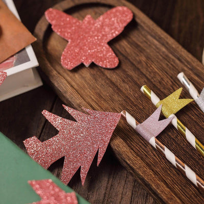 Colorful glitter paper cutouts of a butterfly and holiday tree on a wooden tray.