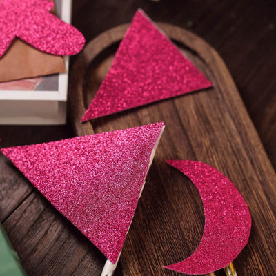Pink glitter shapes in triangle and crescent designs on a wooden surface.