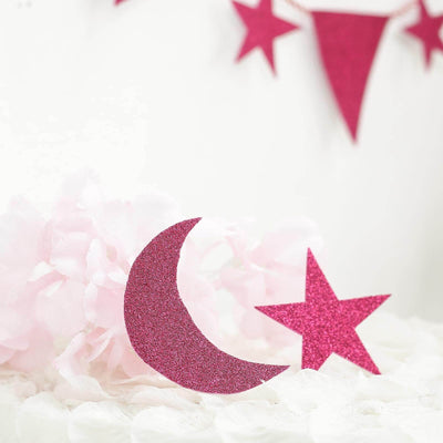 Pink glitter moon and star decorations on a soft backdrop.
