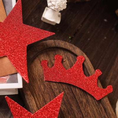 Red glitter crown and star decorations on a wooden surface.