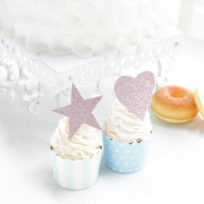 Cupcakes with pink glitter star and heart toppers on a white table.