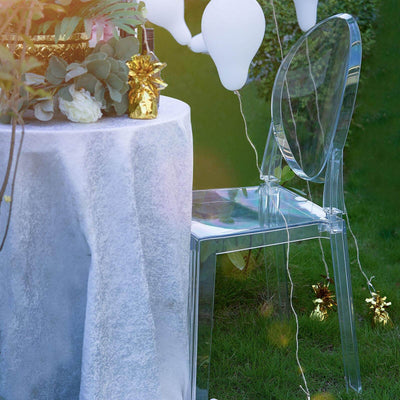 Clear acrylic chair beside a table with balloons and decorations in a garden setting.