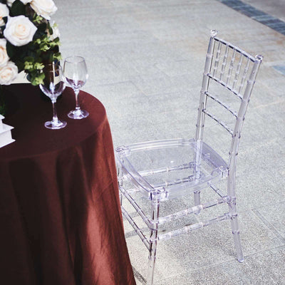 Clear acrylic chiavari chair beside a table with a burgundy tablecloth.