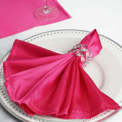 Pink satin napkin elegantly folded with a jeweled napkin ring on a white plate.